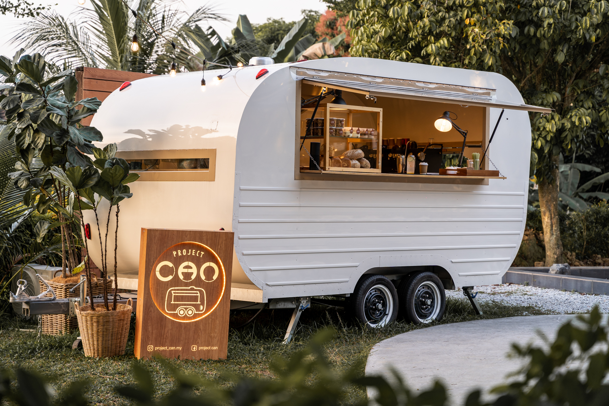 Project CAN's caravan café at golden hour, surrounded by greenery and string lights.